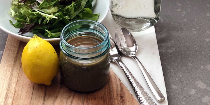 Balsamic Vinaigrette plated on a round mason jar on top of a wood and marble tray next to silverware and fresh produce