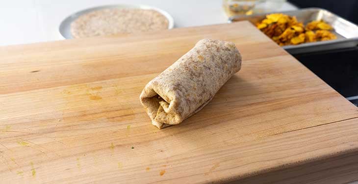 Folded burrito placed on a wooden cutting board