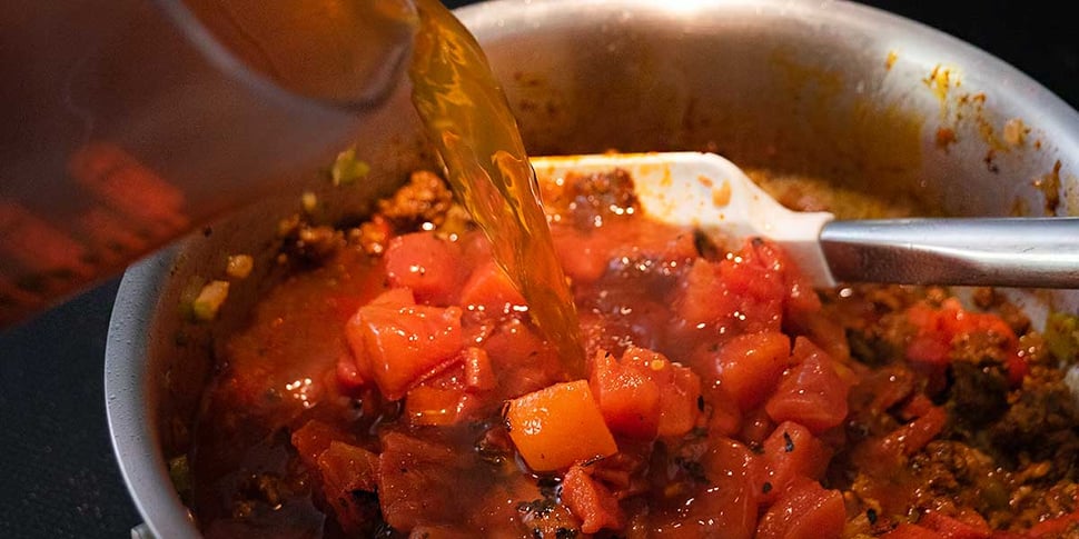 Stock being added to keto chili pan along with diced tomatoes