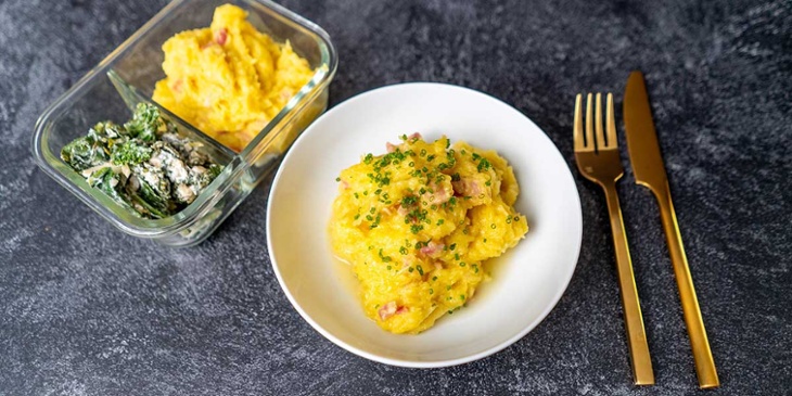 Creamy Bacon and Spaghetti Squash plated on a white bowl and glass container next to golden silverware