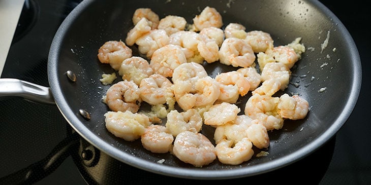 Shrimp added to previously sauteed garlic in a non-stick pan on an electric stovetop