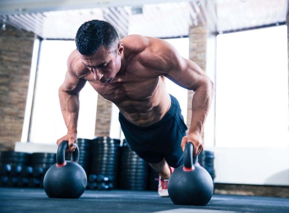 Handsome muscular man doing push ups on kettle ball in crossfit gym