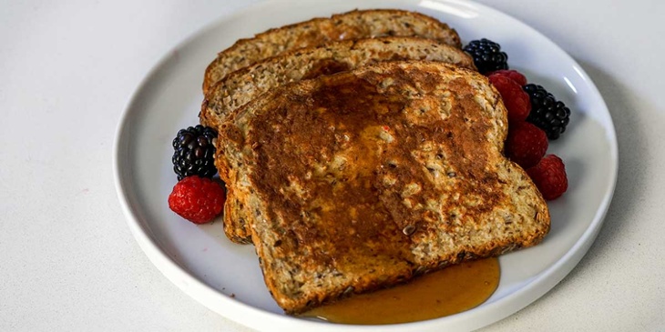 High protein french toast recipe plated with fresh berries and syrup on a white plate