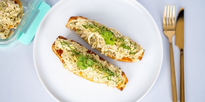 Paleo Chicken Pesto Stuffed Sweet Potato placed on a white plate and meal prep container next to silverware